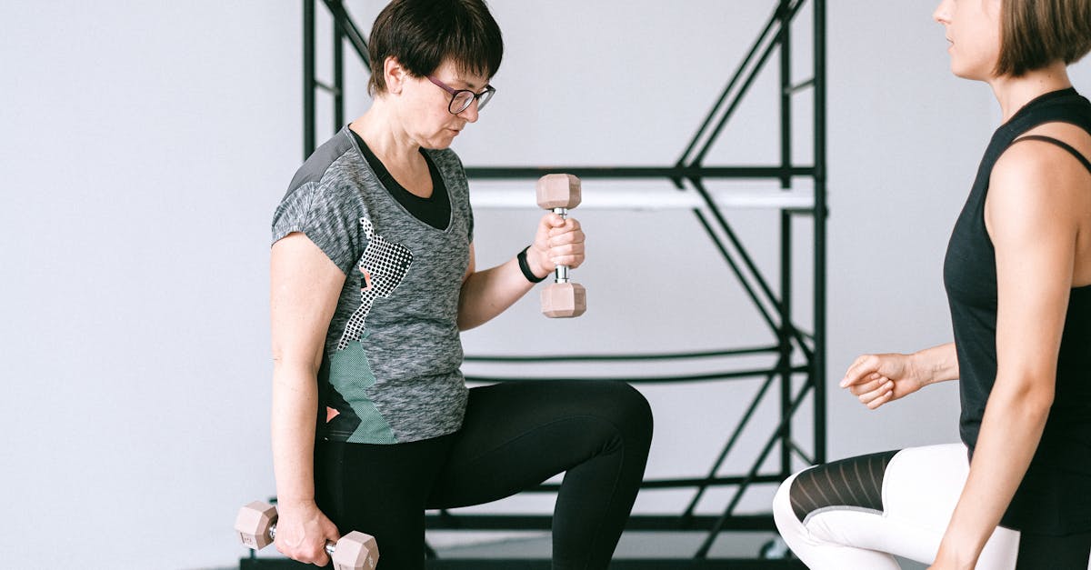 Elderly woman lifting dumbbells with guidance from a trainer indoors.
